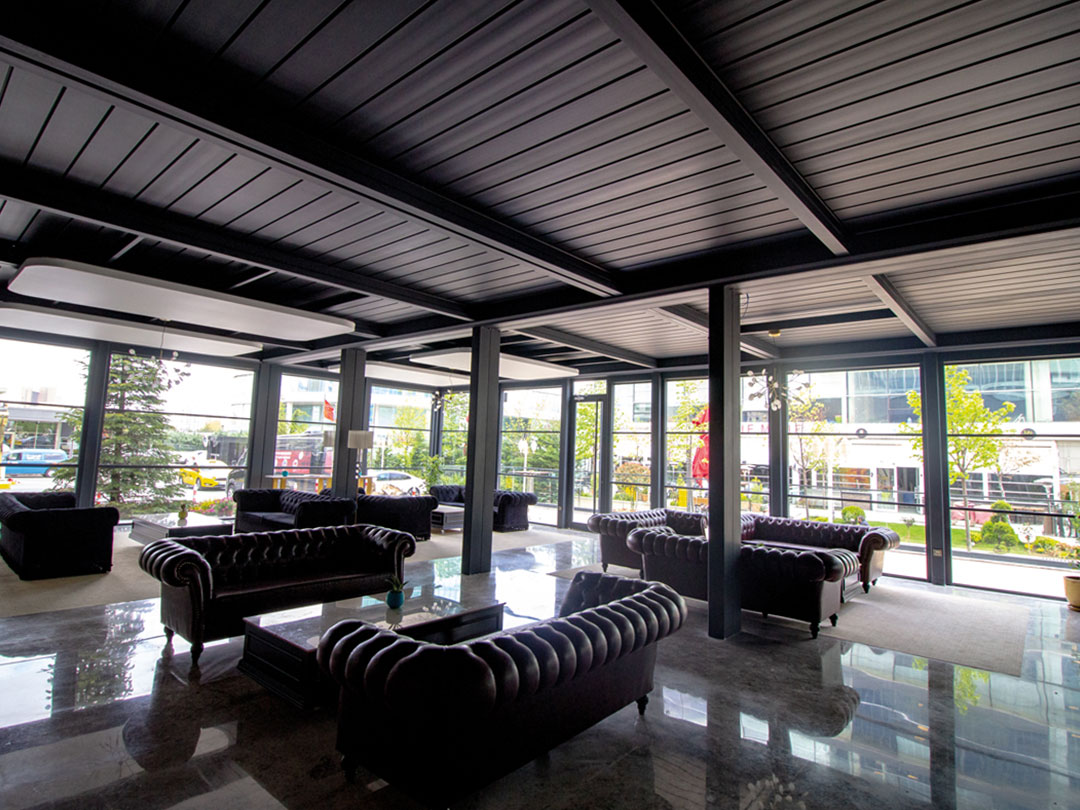 Lobby lounge d’hôtel aménagé sous pergola bioclimatique avec baies vitrées