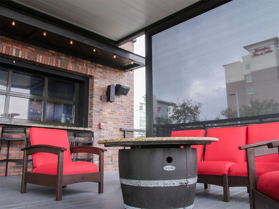 Espace lounge extérieur de bar aménagé sous pergola bioclimatique avec pare-soleil