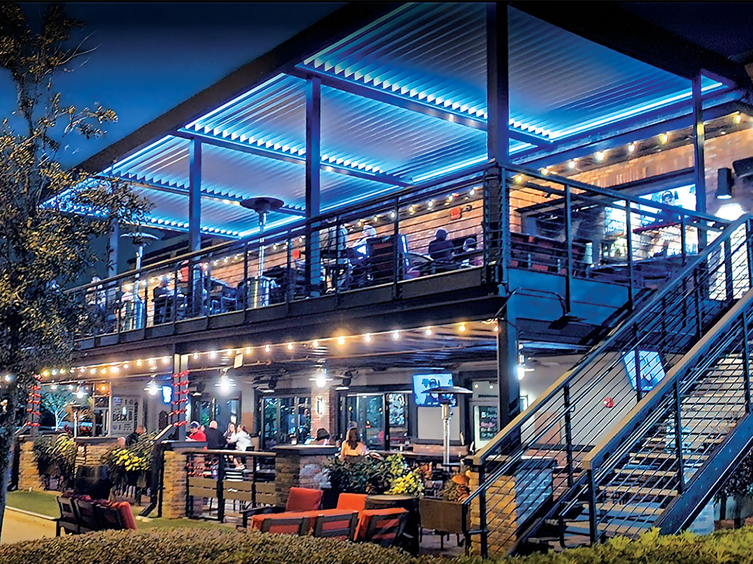 Terrasse de bar avec pergola bioclimatique et éclairage LED bleu en soirée