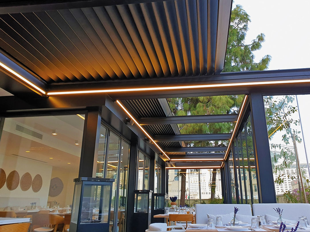 Pergola bioclimatique à lames orientables et rétractables installée sur la terrasse vitrée d’un restaurant